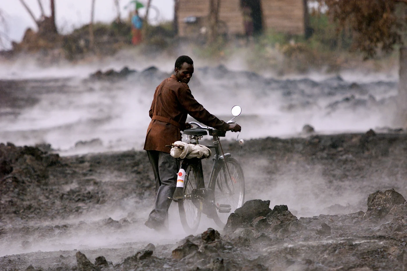 Un congoleño empuja su bicicleta entre los restos humeantes de roca de lava tras una tormenta en la ciudad de Goma, al este del Congo. Foto: AP.